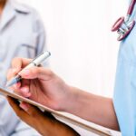 A doctor wearing a white medical lab coat and a dark blue scrub and a stethoscope explaining plan of care and test prescription to the elderly patient